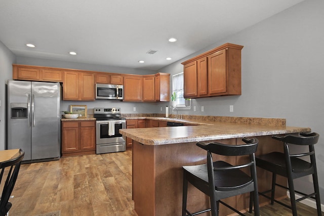 925 Kelli Ct, Centralia, MO 65240 - kitchen with appliances with stainless steel finishes, a peninsula, brown cabinetry, light wood-style flooring, and recessed lighting