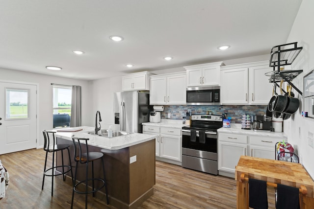 506 Addie Ln, Centralia, MO 65240 - kitchen featuring appliances with stainless steel finishes, backsplash, white cabinetry, an island with sink, and wood finished floors