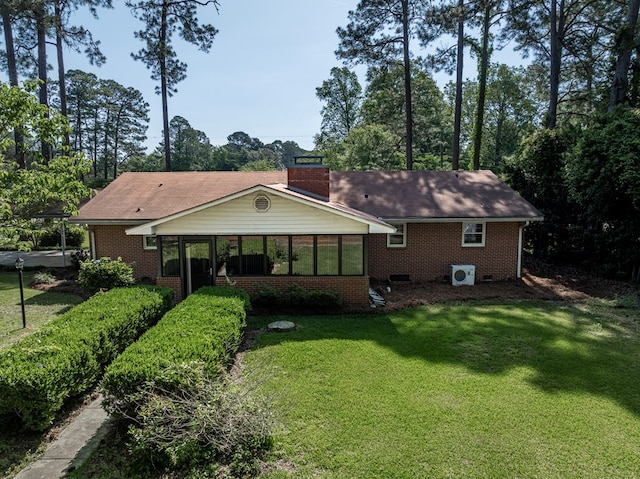 back of house with a lawn, a chimney, a sunroom, and brick siding