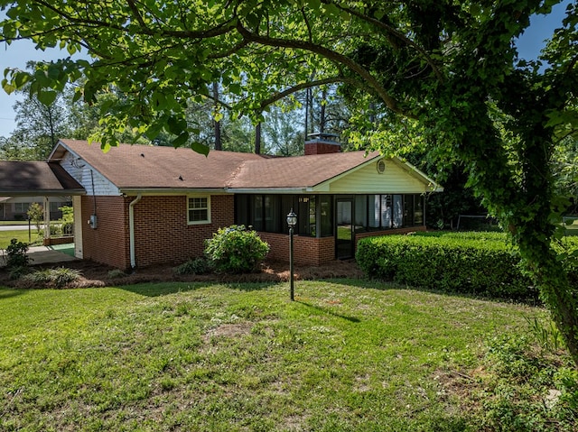exterior space with a sunroom, a chimney, a front lawn, and brick siding