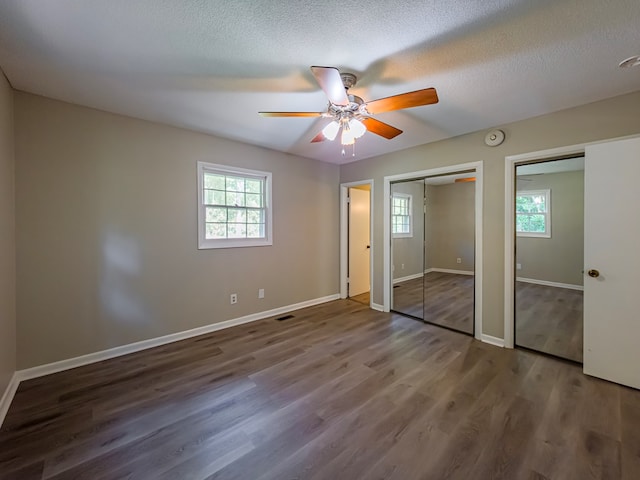 unfurnished bedroom with two closets, ceiling fan, wood finished floors, and baseboards