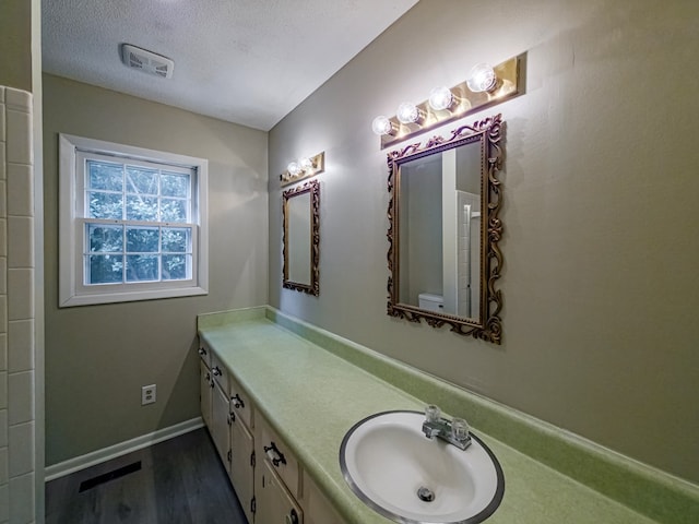 full bath featuring a textured ceiling, visible vents, baseboards, wood finished floors, and vanity