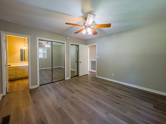 unfurnished bedroom featuring wood finished floors, two closets, visible vents, and baseboards
