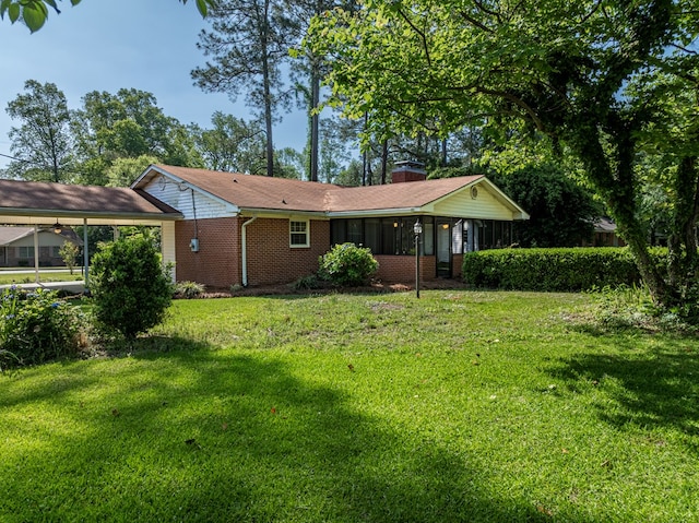 rear view of house featuring a lawn, a chimney, brick siding, and a carport