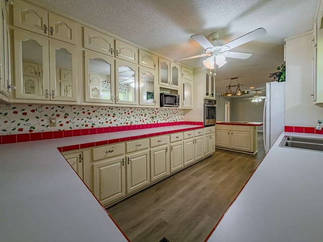 kitchen with a sink, cream cabinets, a ceiling fan, appliances with stainless steel finishes, and wood finished floors