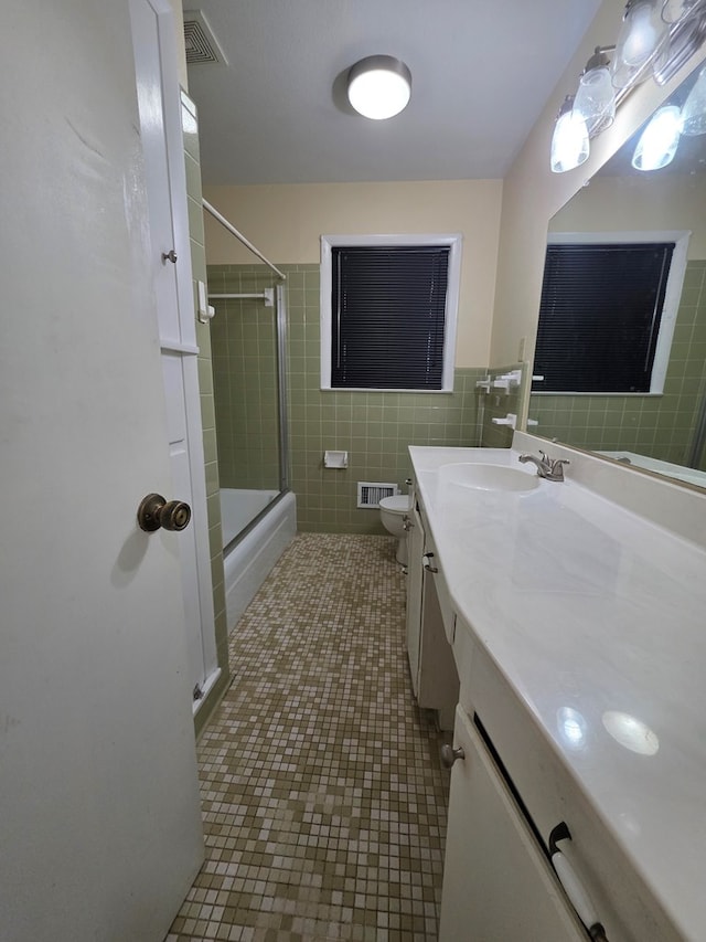 full bath featuring visible vents, vanity, toilet, tile walls, and enclosed tub / shower combo
