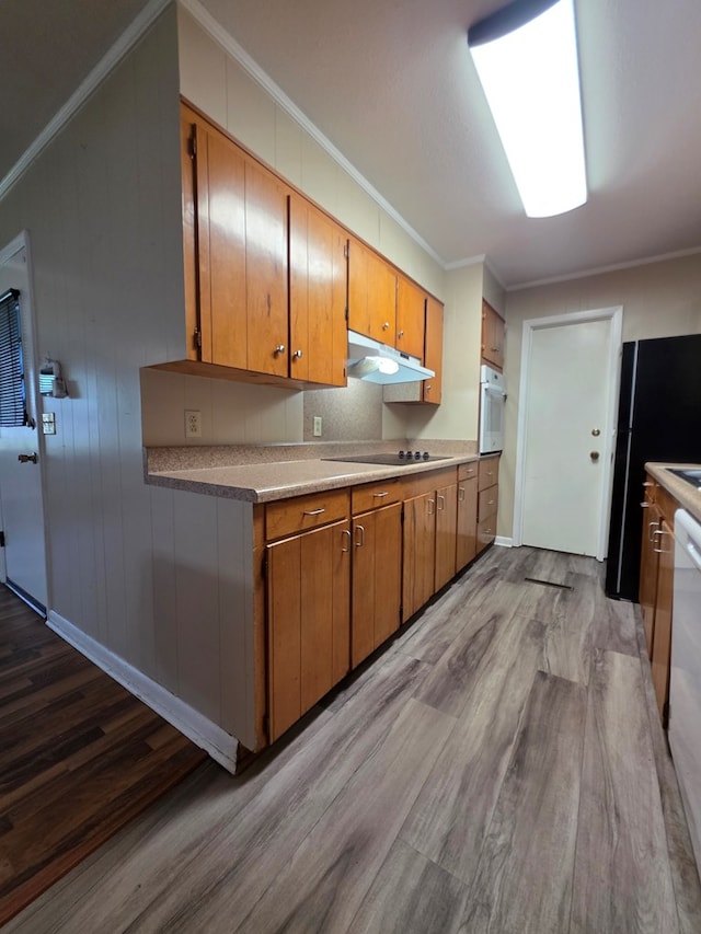 kitchen with brown cabinets, crown molding, wood finished floors, under cabinet range hood, and black appliances