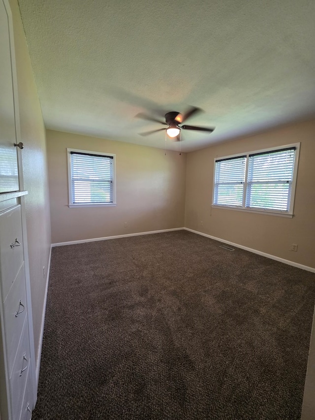 empty room with baseboards, ceiling fan, dark carpet, and a wealth of natural light