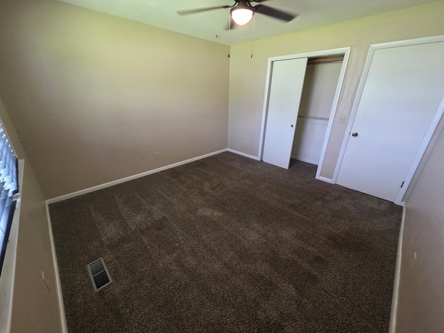 unfurnished bedroom featuring visible vents, a closet, baseboards, dark carpet, and ceiling fan
