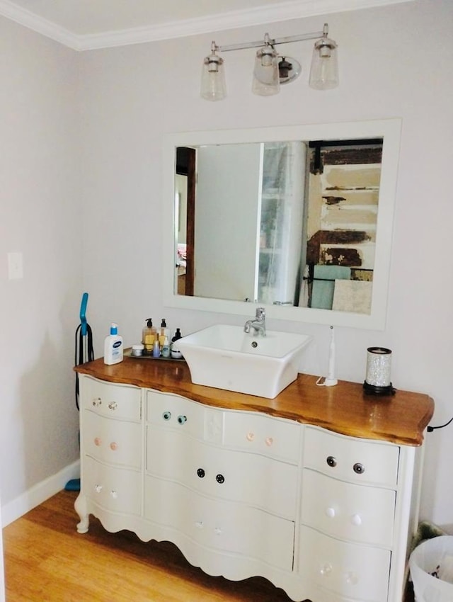 bathroom with baseboards, wood finished floors, crown molding, and vanity