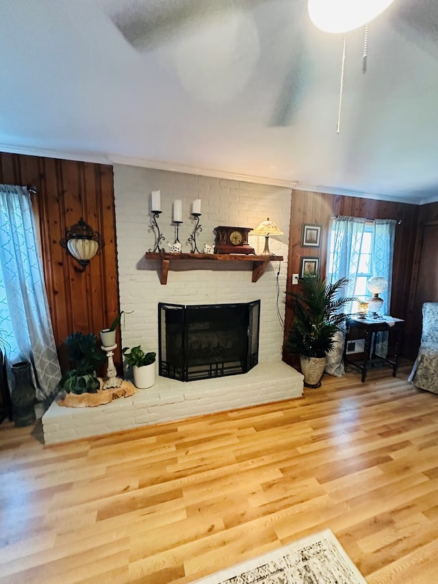 living area featuring wood finished floors, wooden walls, ornamental molding, and a brick fireplace