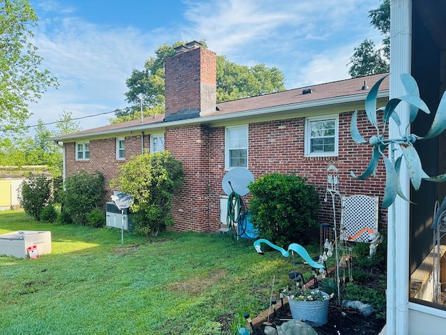 back of house featuring a lawn, brick siding, and a chimney