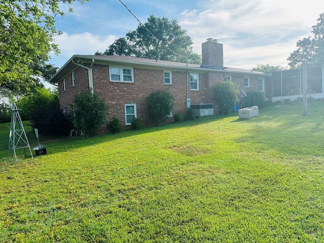 rear view of property with brick siding, a yard, and a chimney