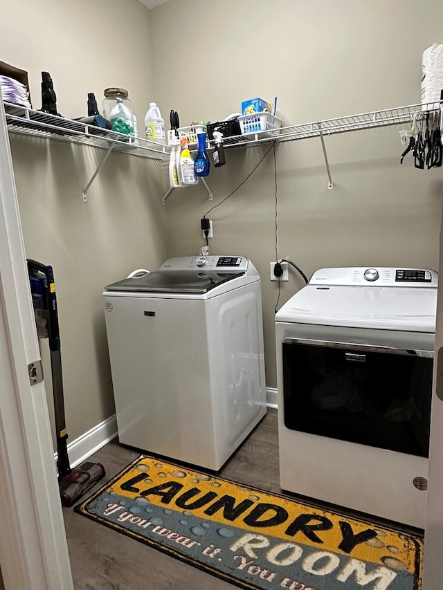 clothes washing area featuring laundry area, baseboards, washing machine and dryer, and wood finished floors