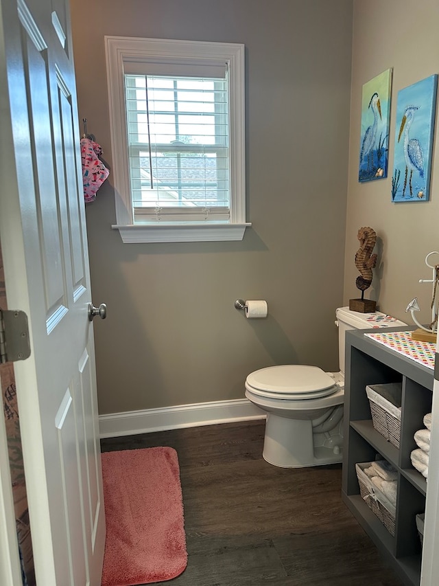 half bathroom with baseboards, wood finished floors, and toilet