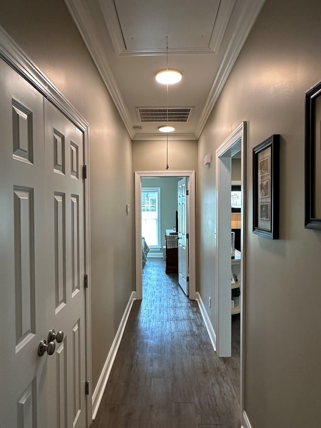 hall with attic access, visible vents, dark wood finished floors, baseboards, and ornamental molding