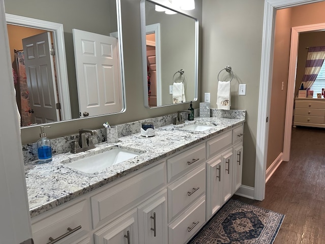 bathroom with double vanity, a sink, baseboards, and wood finished floors