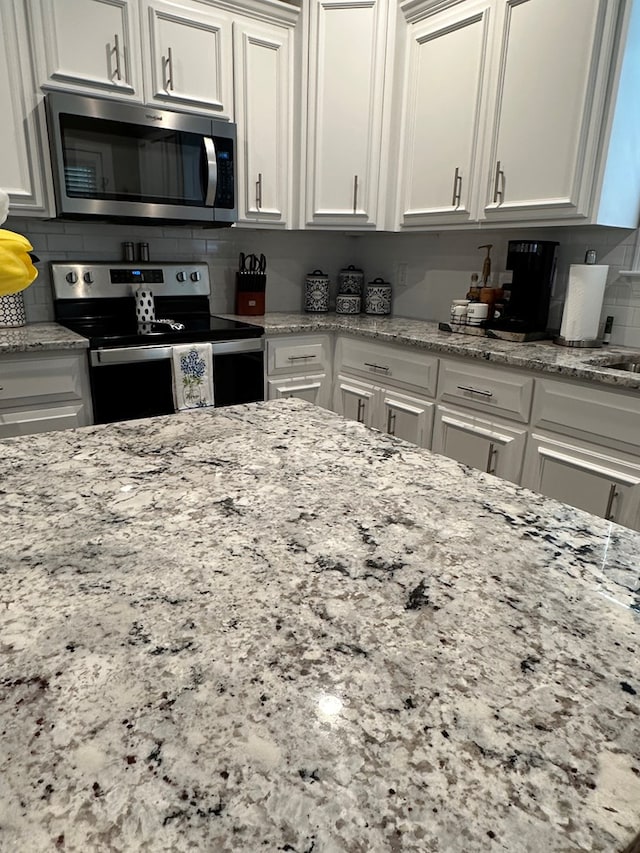 kitchen featuring backsplash, stainless steel appliances, light stone counters, and white cabinetry