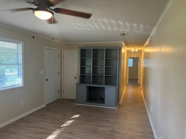 interior space featuring baseboards, a textured ceiling, crown molding, visible vents, and wood finished floors