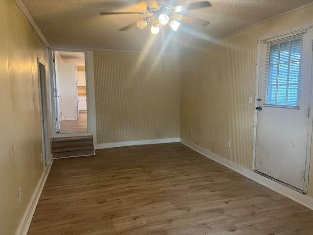 spare room featuring crown molding, a textured ceiling, a ceiling fan, wood finished floors, and baseboards