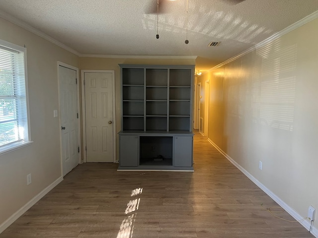 unfurnished living room featuring baseboards, a textured ceiling, ornamental molding, and wood finished floors