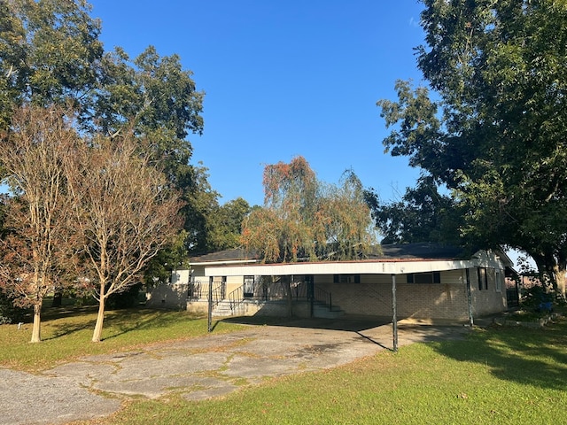 back of house featuring brick siding, a carport, driveway, and a lawn