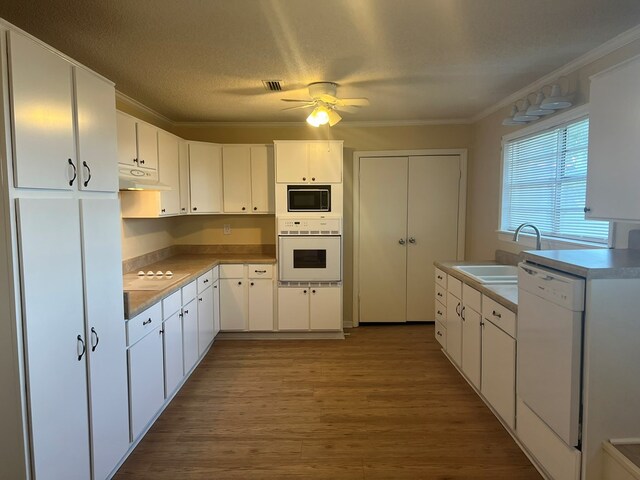 kitchen with white appliances, crown molding, under cabinet range hood, a sink, and wood finished floors