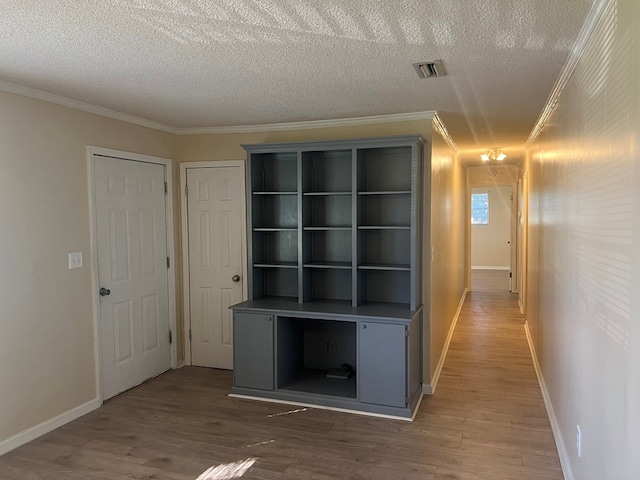 corridor with a textured ceiling, wood finished floors, ornamental molding, and visible vents