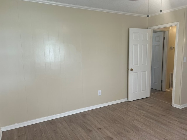 empty room featuring crown molding, visible vents, baseboards, and wood finished floors