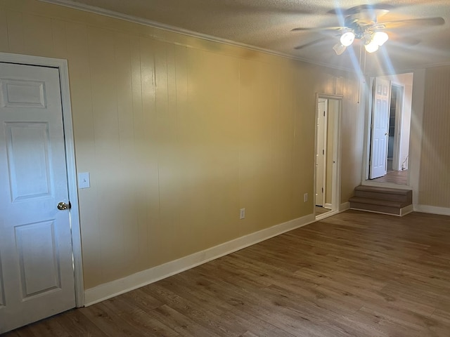 spare room with baseboards, ceiling fan, a textured ceiling, crown molding, and wood finished floors