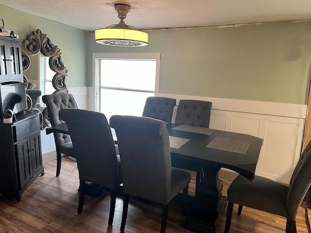 dining area with dark wood-type flooring, a textured ceiling, and a wainscoted wall