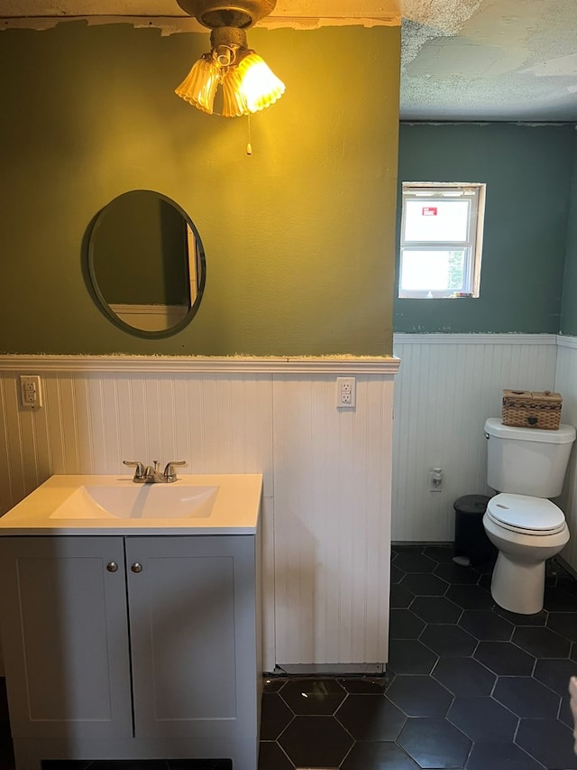 bathroom featuring vanity, tile patterned floors, a textured ceiling, toilet, and wainscoting