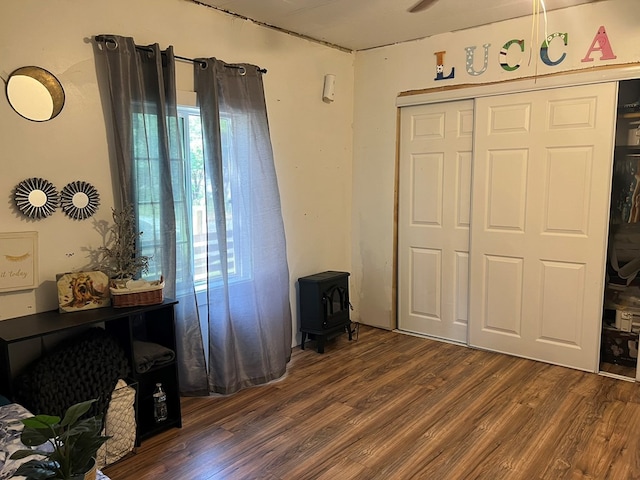 bedroom with a closet, a wood stove, dark wood-style flooring, and multiple windows