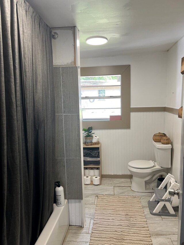 full bath featuring toilet, shower / tub combo, a wainscoted wall, and wood finished floors
