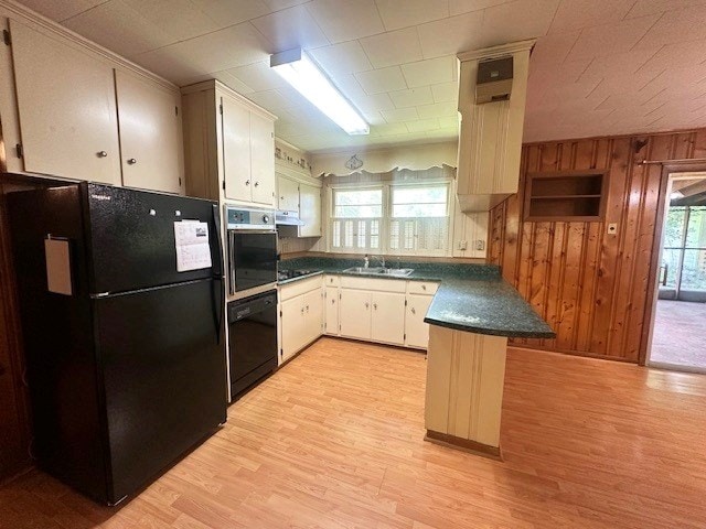 237 Dewey Mcglamry Rd, Fitzgerald, GA 31750 - kitchen with black appliances, dark countertops, a peninsula, light wood-type flooring, and wooden walls