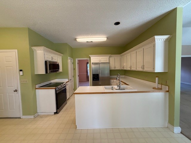 218 Sutton Rd, Tifton, GA 31794 - kitchen featuring appliances with stainless steel finishes, a peninsula, white cabinetry, light floors, and a textured ceiling