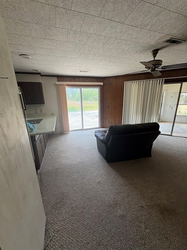 carpeted living area with wooden walls, a ceiling fan, and visible vents