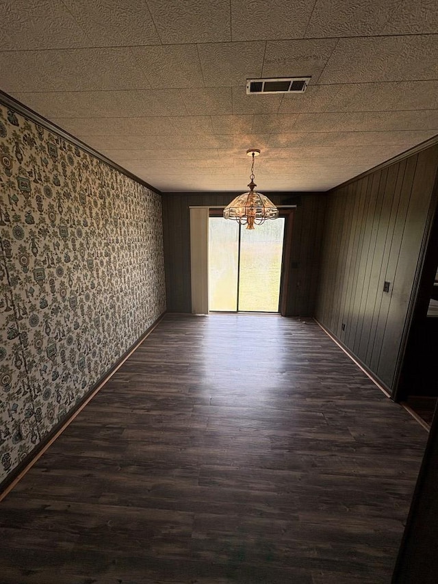 unfurnished dining area featuring wallpapered walls, an inviting chandelier, dark wood-style floors, and visible vents