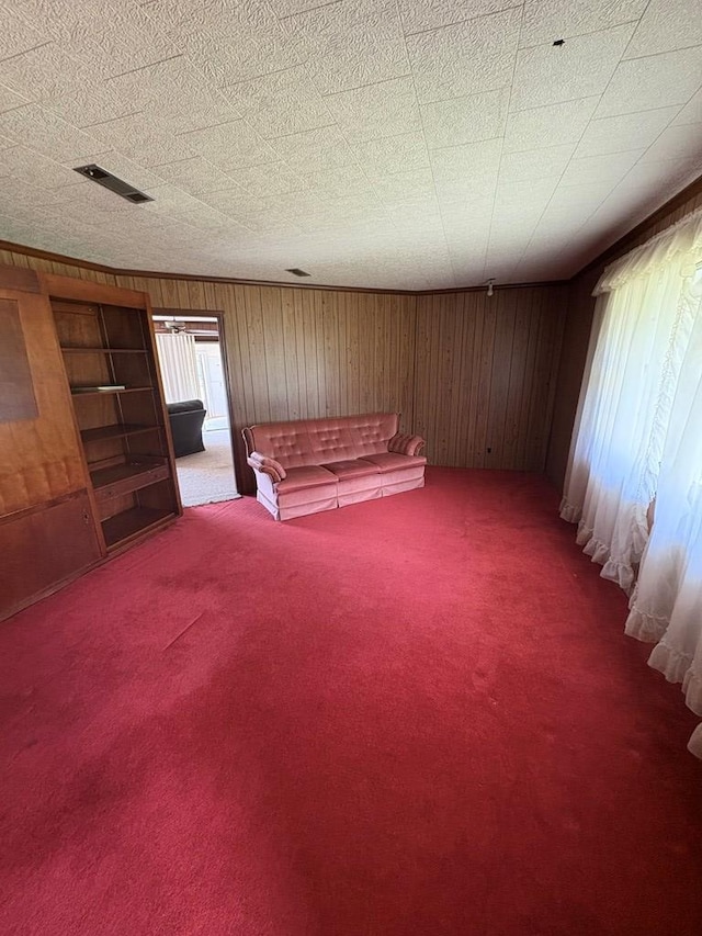 unfurnished living room featuring wooden walls, carpet flooring, and visible vents