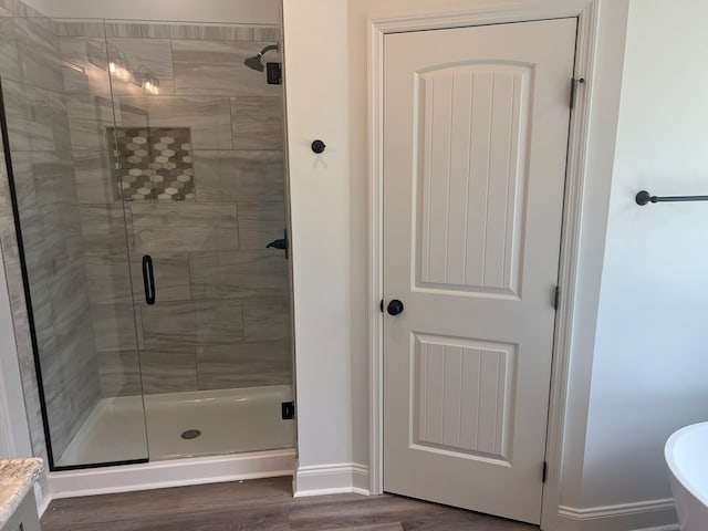 full bathroom featuring baseboards, wood finished floors, and a stall shower