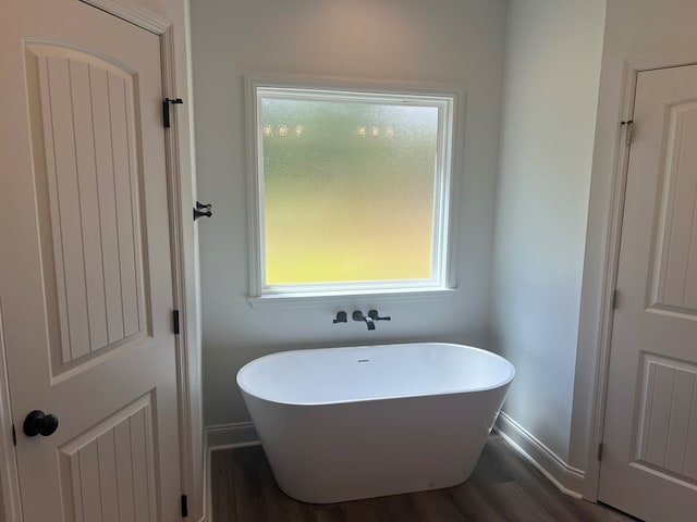 full bathroom featuring baseboards, a freestanding tub, wood finished floors, and a wealth of natural light