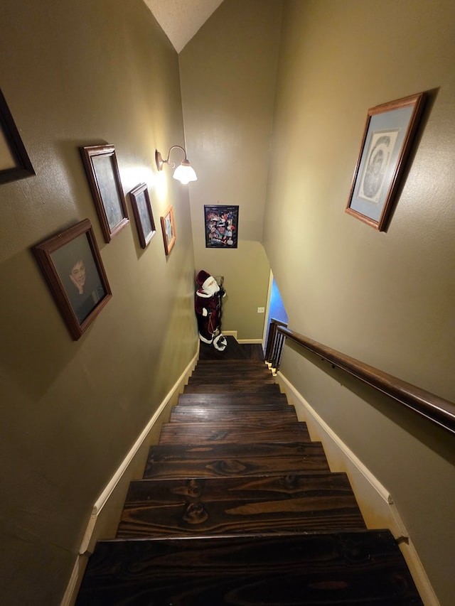 stairs with wood finished floors, baseboards, and lofted ceiling