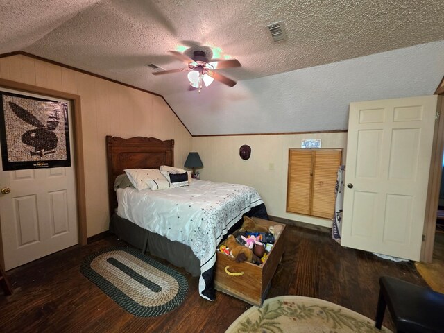 bedroom with vaulted ceiling, a textured ceiling, wood finished floors, ceiling fan, and wooden walls