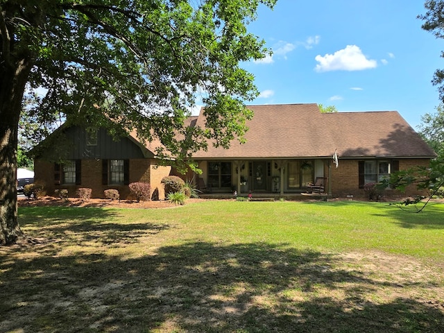 rear view of property featuring a yard, brick siding, and a porch