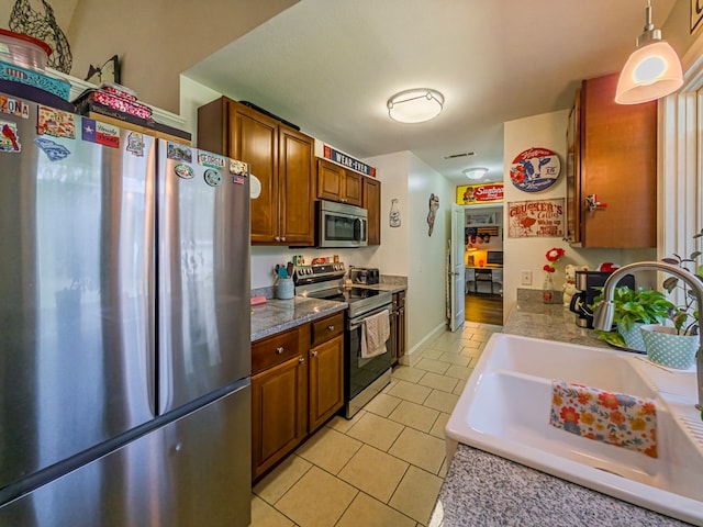 127 Carol Cir, Fitzgerald, GA 31750 - kitchen featuring appliances with stainless steel finishes, light tile patterned floors, brown cabinetry, and hanging light fixtures