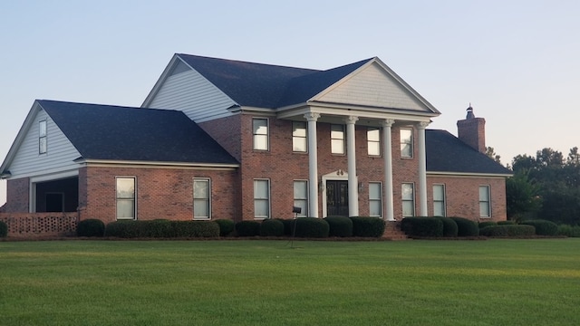 neoclassical / greek revival house with a chimney, a front yard, and brick siding