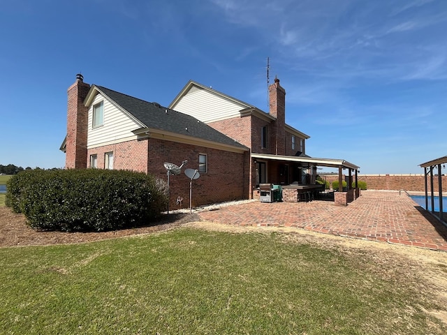 back of house with a lawn, a patio area, fence, brick siding, and a chimney