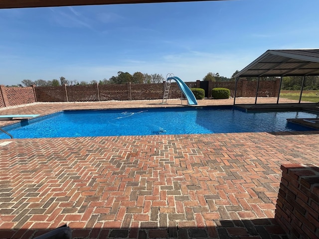 view of swimming pool with a water slide, fence private yard, a diving board, and a fenced in pool