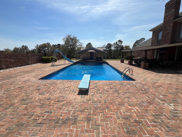 view of pool featuring a diving board, a water slide, fence, a patio, and a fenced in pool