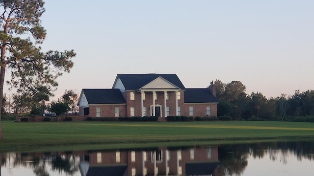 neoclassical home featuring a front lawn and a water view